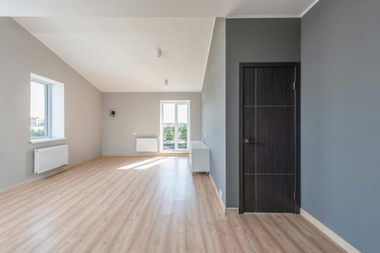 Spacious empty room with wooden flooring and large windows for ample natural light.