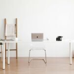 Bright and minimalist home office setup with a white desk, laptop, and potted plant.